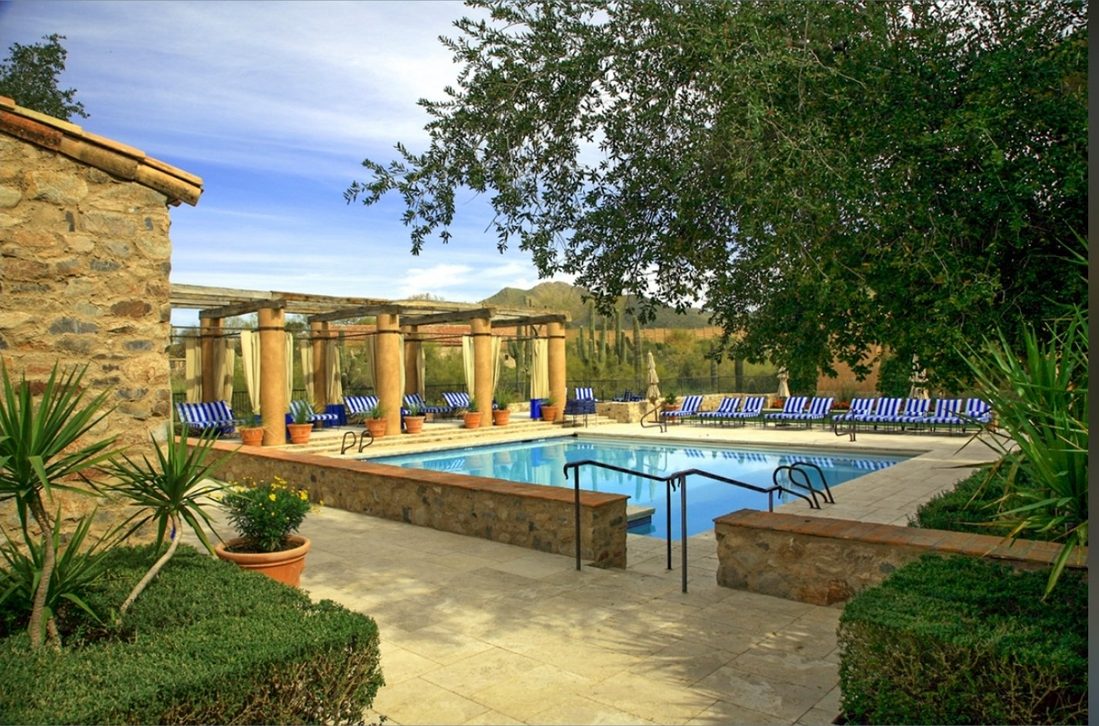 The Silverleaf Club pool deck — a pergola with draped cabanas, striped lounge chairs and the pool, desert greenery and mountains beyond