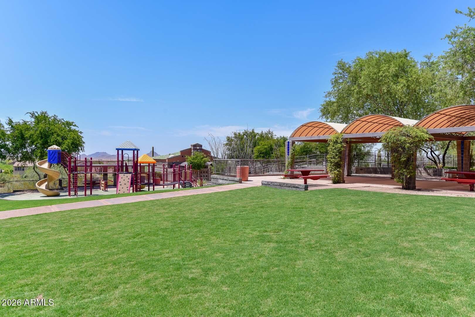 Playground, shaded picnic ramadas and a broad lawn at a Tramonto community park under a clear blue sky